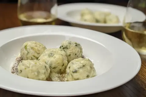 En tallrik med fluffiga gnudi, perfekt för ett enkelt gnudi recept. Serveras med riven ost och ett glas vitt vin.