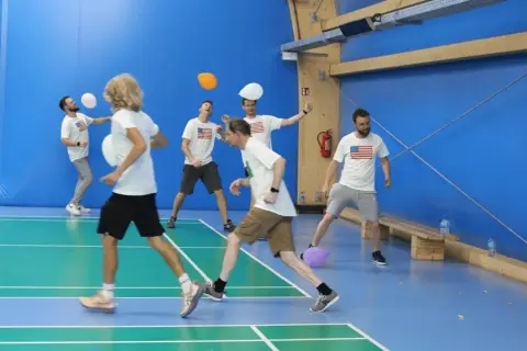 Mężczyźni w koszulkach z amerykańską flagą bawią się balonami na sali gimnastycznej. To świetna integracja dla dorosłych!