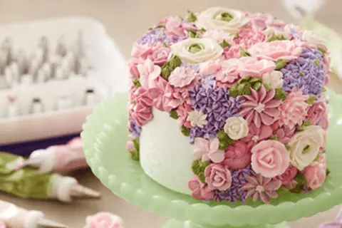 En tårta täckt av vackra blommor skapade genom att spritsa tårta med frosting i rosa, lila och gröna nyanser.