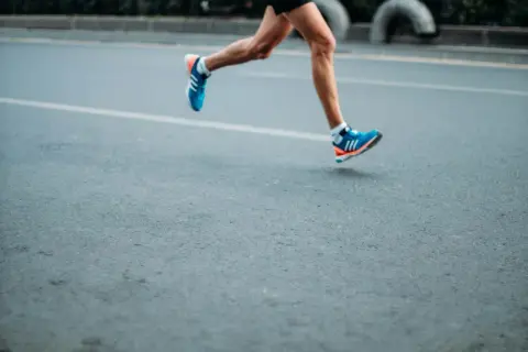 A runner's legs in motion, wearing blue and orange sneakers. This image evokes the dedication required to train, making one wonder how many miles do boxers run to achieve peak fitness.