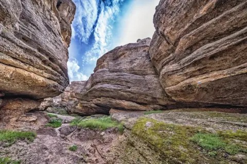 Sendero entre imponentes rocas erosionadas, con el cielo azul y nubes blancas asomando. Un paisaje que evoca la grandeza de los Picos de Urbión.