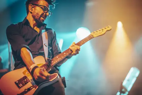 Muzyk w okularach gra na gitarze, otoczony światłami sceny. Jego gra to prawdziwa **farben lehre** dźwięków i emocji.