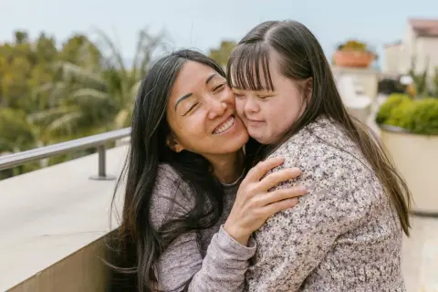 Abbraccio affettuoso tra due donne, una con sindrome di Down, che condividono un momento di gioia e amore.