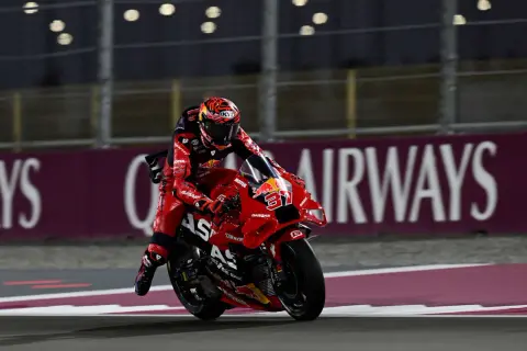 Piloto de MotoGP con traje rojo y casco a juego, en plena carrera. Busca sumar puntos en la clasificación.