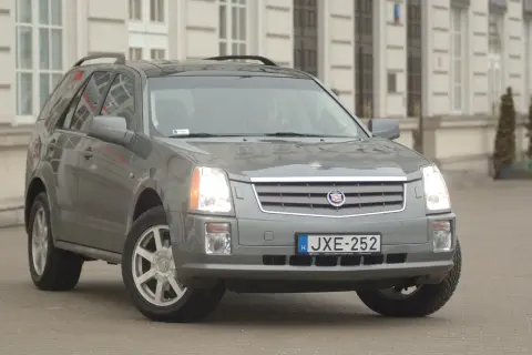 Szary Cadillac SRX z tablicą rejestracyjną JXE-252 zaparkowany przed budynkiem.