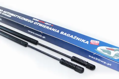 Dwa siłowniki do automatycznego otwierania bagażnika, zapakowane w niebieskie pudełko z napisem "MADE IN POLAND".