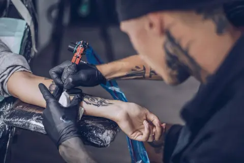 Ein Mann erhält ein intimtattoo am Arm. Der Tätowierer arbeitet sorgfältig mit der Maschine.