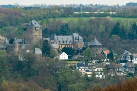 Zamek Schloss Burg w Solingen, otoczony zielenią, z wieżami i budynkami mieszkalnymi u podnóża.