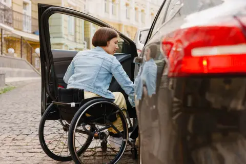 Donna in carrozzina si avvicina all'auto. Scopri lo sconto assicurazione auto legge 104 per una maggiore libertà di movimento.