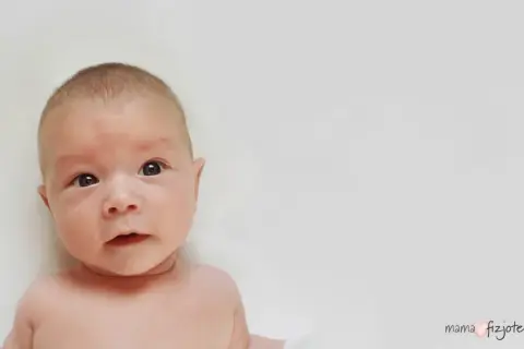 Urocze roczne dziecko przechyla głowę do ramienia, patrząc z zaciekawieniem.