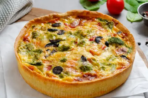 Une délicieuse quiche au poulet, garnie de brocolis, d'olives et de poivrons, prête à être dégustée.