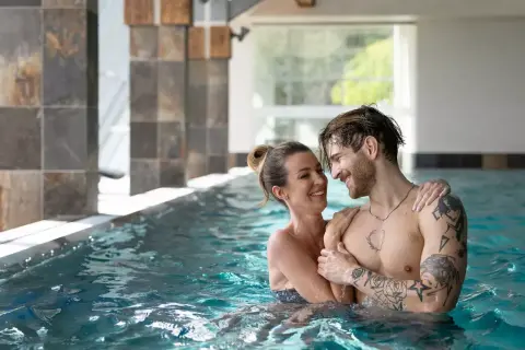 Para w basenie SPA, uśmiechnięci, patrzą na siebie.