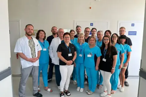 Grupa pracowników medycznych w niebieskich i białych uniformach stoi w korytarzu.