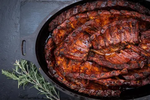 Saftige spareribs im Dutch Oven, glasiert und bereit zum Genießen. Ein Rosmarinzweig liegt daneben.