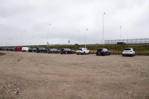 Rząd samochodów na parkingu, w tym czerwony van i białe SUV-y. Zastanawiasz się, ile kosztuje parking na lotnisku w Warszawie?