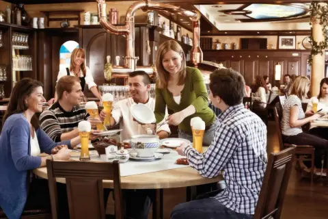 Gäste genießen Bier und Essen im Erdinger Brauhaus. Eine Kellnerin serviert, während Freunde lachen und trinken.