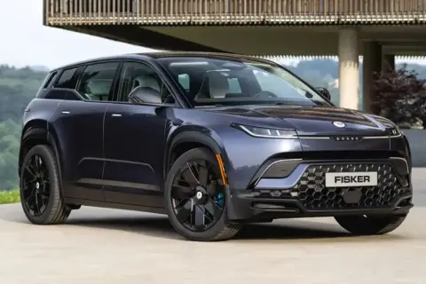 Fisker Ocean, un SUV eléctrico azul oscuro, aparcado frente a una casa moderna con vistas a un bosque.