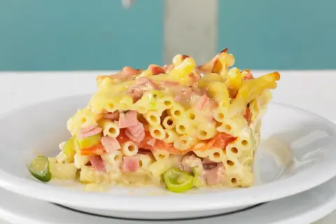 Ein Stück saftiger Makkaroni Auflauf mit Schinken, Gemüse und Käse, serviert auf einem weißen Teller.