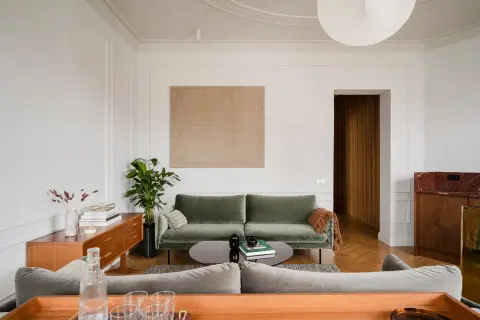Disposizione divani salotto: un divano verde salvia e uno grigio creano un angolo conversazione accogliente, con un tavolino basso e un mobile vintage.