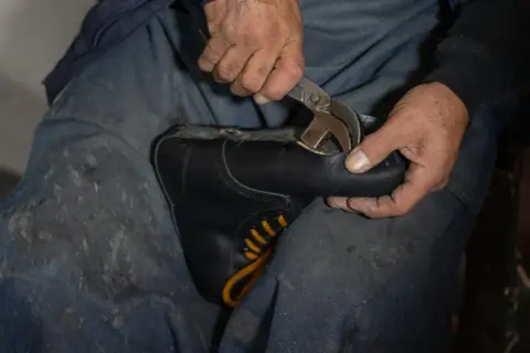 Mains d'un cordonnier travaillant sur une chaussure simili cuir qui s'effrite, utilisant une pince pour la réparer.