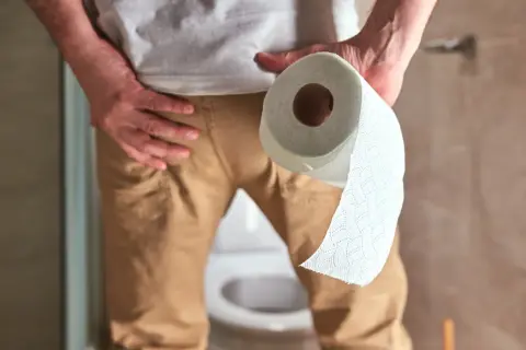 Mężczyzna trzymający rolkę papieru toaletowego, symbolizująca prawidłowe oddawanie moczu u mężczyzn i higienę.