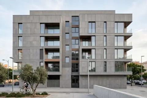 Edificio moderno con revestimiento fachada ventilada de piedra gris, balcones acristalados y detalles en madera. Un ciclista pasa frente a los olivos.