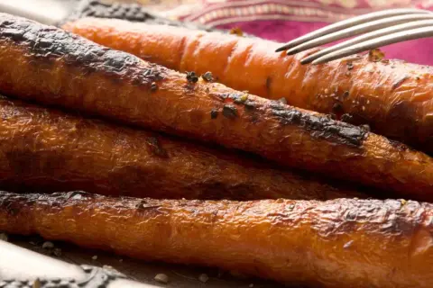 Carottes rôties, caramélisées et légèrement grillées, servies sur une assiette avec une fourchette. Un délice croustillant et savoureux.