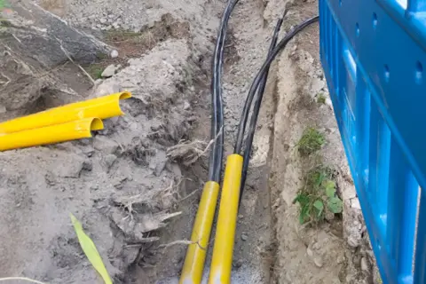 Kabel elektryczny w ziemi, chroniony żółtymi osłonami, przygotowany do zakopania zgodnie z przepisami.