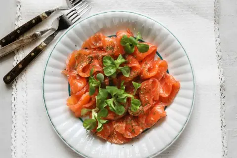 Vacker tallrik med gravad lax, garnerad med dill och gröna blad. Frågan är om man kan frysa gravad lax för att spara den till senare.