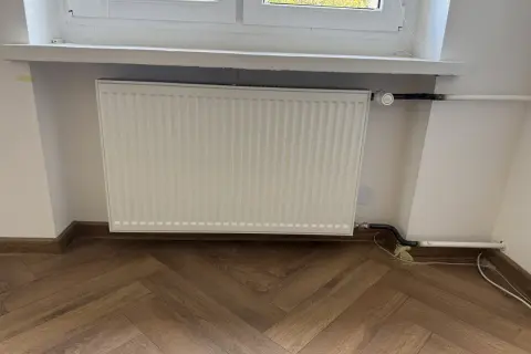 Biały grzejnik pod oknem, nowe podłączenie. Zastanawiasz się, ile kosztuje wymiana kaloryfera?