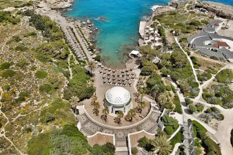 Vacker vy över Kallithea Beach med turkost vatten, solstolar och en kupolformad byggnad.