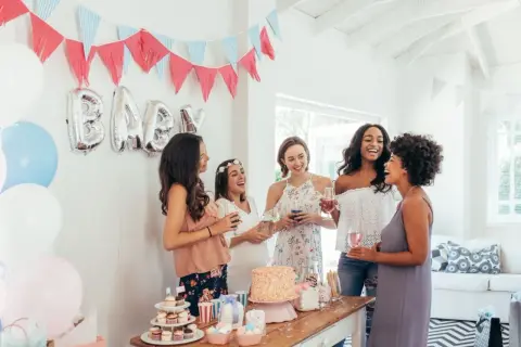 Radosne kobiety świętują baby shower. Balony z napisem "BABY", girlandy i tort tworzą atmosferę. To idealne miejsce, by dowiedzieć się, baby shower co to jest!