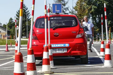 Czerwony Hyundai na placu manewrowym, gotowy do egzaminu na prawo jazdy B. Instruktor pokazuje znak zwycięstwa.