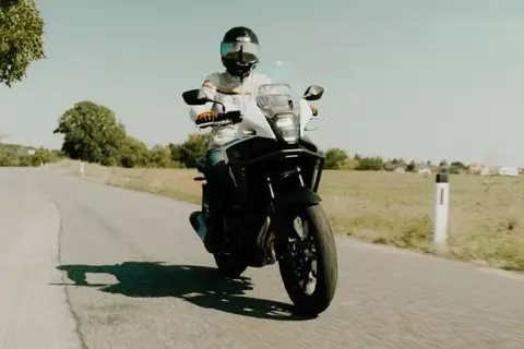 Motocyklista w kasku jedzie motocyklem turystycznym po wiejskiej drodze. Idealny na kategorię A2.