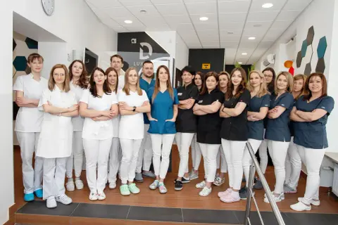 Zespół stomatologów w białych i granatowych uniformach stoi w gabinecie.