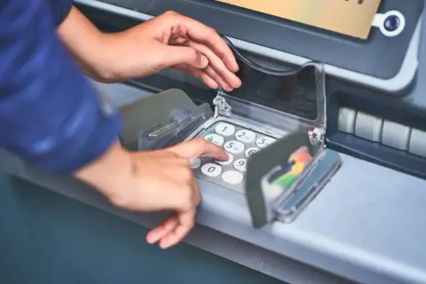 Dłoń wprowadza PIN do bankomatu, pokazując, jak włożyć kartę do bankomatu i dokonać transakcji.