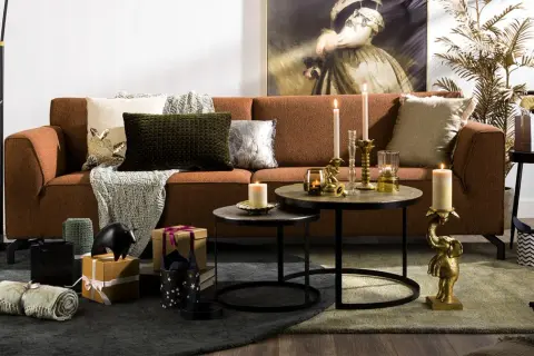 Salon chaleureux avec canapé rouille, coussins texturés et décorations dorées. L'ambiance est réconfortante, avec des touches de **couleur cooper** apportées par des bougies et des statuettes d'éléphants.