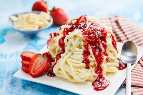 Ein köstliches Spaghetti-Eis mit Erdbeersoße und frischen Erdbeeren, bereit zum Genießen.
