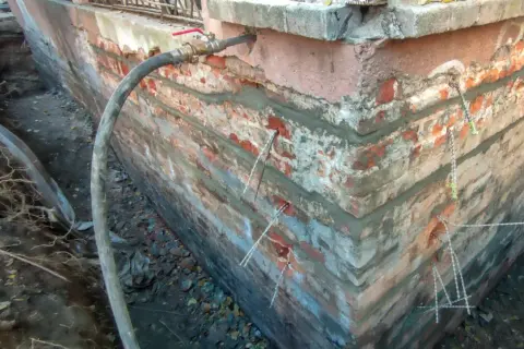 Prace przy fundamentach: wstrzykiwanie zaprawy, by wzmocnić istniejący fundament. Widać węże i elementy kotwiące.
