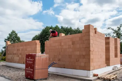 Budowa domu z pustaków ceramicznych Porotherm. Murarz układa kolejne warstwy cegieł.