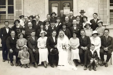 Un groupe de personnes pose pour une photo de mariage. La mariée est au centre, entourée de sa famille et de ses amis. Ce **registre mariage** témoigne d'un jour heureux.