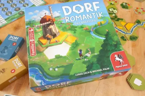 Das Familienspiel des Jahres "Dorfromantik" mit seinen bunten Spielsteinen und der Hauptbox, die eine idyllische Landschaft mit Windmühle zeigt.