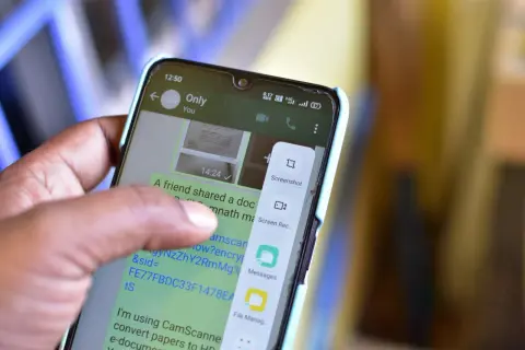 Palec dotyka ekranu telefonu, wybierając opcję "Screenshot", aby pokazać, jak zrobić screena.