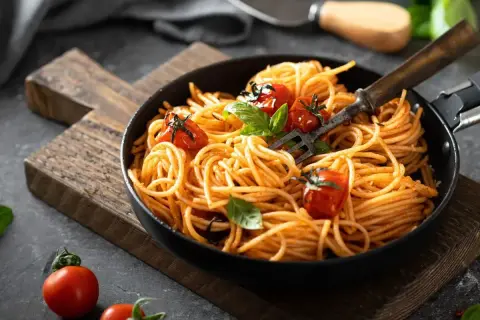 Szybki obiad z makaronem spaghetti w sosie pomidorowym, udekorowany pomidorkami koktajlowymi i bazylią. Idealny na każdy dzień.