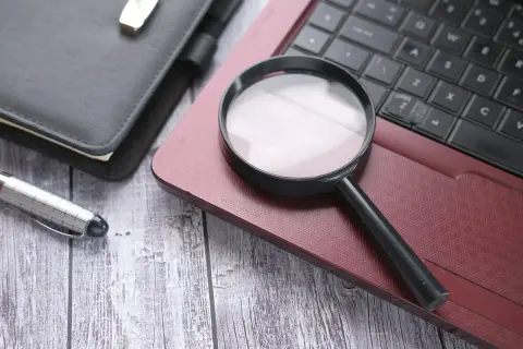 Lupa na klawiaturze laptopa, obok notatnika i długopisu. Jak sprawdzić model laptopa?