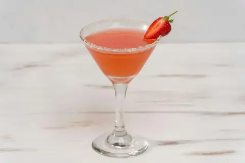 En rosa strawberry daiquiri i ett martiniglas med socker på kanten och en jordgubbsklyfta som garnering.