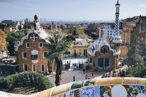 Bunte Mosaike und märchenhafte Gebäude im Park Güell, ein Wahrzeichen von Barcelona. Die Skyline der Stadt im Hintergrund.