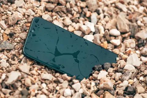 Smartfon leży na kamieniach, mokry, ale wytrzymały zgodnie ze **standardem militarnym MIL-STD-810H**.