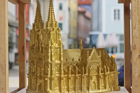 Goldene Nachbildung des Regensburger Doms mit filigranen Figuren und Türmen, die vor einer unscharfen Stadtkulisse steht.