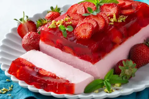 Pyszny sernik na zimno z galaretką i truskawkami, udekorowany miętą i pistacjami. Idealny na letnie popołudnie.
